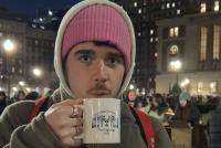 Porträt des Stipendiaten Julius mit Kapuze; er hält einen weißen Becher mit der Aufschrift „Columbia University - Tree Lighting 2025“ bei einer Abendveranstaltung auf dem Campus.