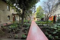 Ein roter Steg führt durch einen Garten zwischen Hochschulgebäuden.