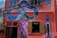 Das Bild zeigt ein rotes Haus mit buntem Mural auf einer Straße in Hanglage in Valparaiso. Der Himmel darüber ist strahlend blau.
