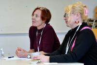 2 Teilnehmerinnen der Staff Week sitzen an einem Tisch und hören intensiv zu.