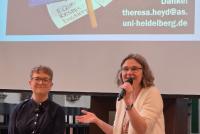 Prof. Dr. Theresa Heyd und Dr. Christiane Wienand bei der Diskussion mit dem Publikum. Im Hintergrund ein Bild, das ein Demoschild mit dem Schriftzug "Protect Trans Students" zeigt.