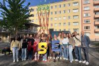 Die Teilnehmenden der Future-Literacies-Projektwoche und Dr. Kristóf Fenyvesi stehen gemeinsam im Freien vor einem selbst gebauten Modell des Warka Water Towers – einer leichten, turmartigen Struktur aus bunten Steckelementen.