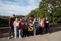Gruppenfoto der Teilnehmenden der Future Literacies-Projektwoche am letzten Tag auf dem historischen Campus „Vanha Seminaarinmäki“ der Universität Jyväskylä. Die Gruppe steht auf der Terrasse des Hauptgebäudes, das von Alvar Aalto entworfen wurde. Im Hintergrund sind herbstliche Bäume zu sehen.