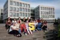 Eine Gruppe von 16 MINT-Lehramtsstudierenden der Universität Heidelberg sitzt in zwei Reihen auf Treppenstufen vor dem modernen Ruusopuisto-Gebäude der Universität Jyväskylä in Finnland. Drei von ihnen halten die bunten Buchstaben „H“, „S“ und „E“ in die Kamera. Das Bild zeigt die Teilnehmenden der ersten Future Literacies-Projektwoche.