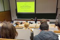 Alexander Mittag vom Zentrum für Schulqualität und Lehrkräftebildung bei seiner Keynote zum neuen Pflichtfach "Informatik und Medienbildung". Im Vordergrund gefüllte Hörsaalreihen.