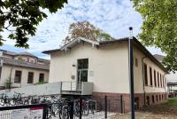 Das HSE-Gebäude in der Voßstraße 2 mit Blick auf den Haupteingang mit Rampe und Fahrradständer, gerahmt vom begrünten Campus Bergheim..